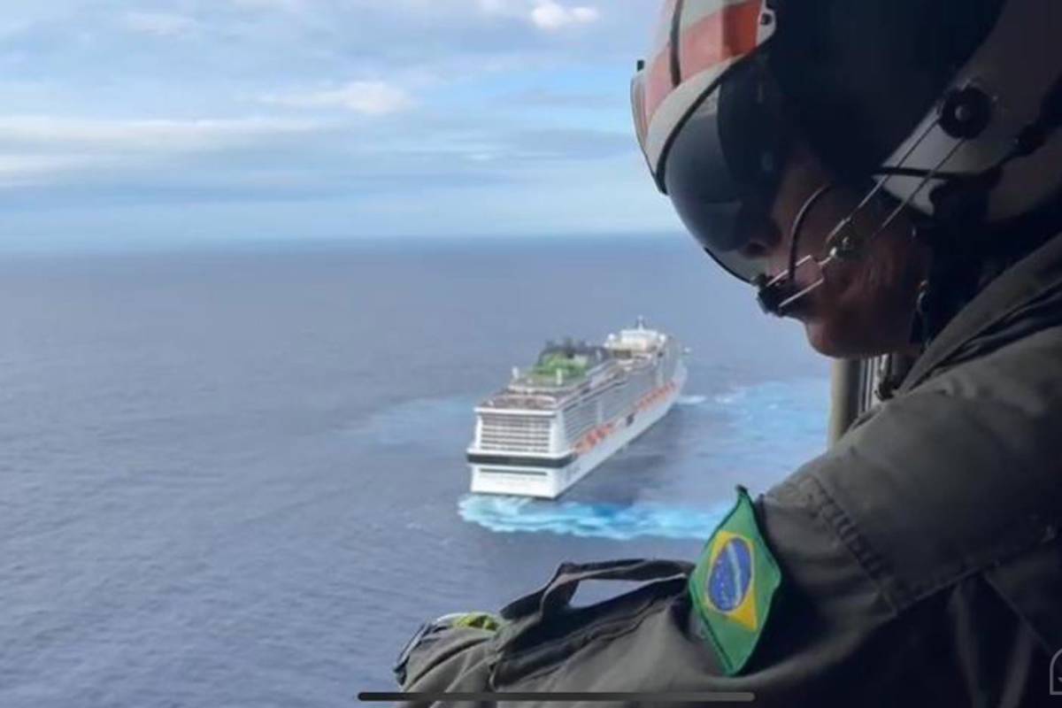 Militar da Marinha do Brasil a bordo do helicóptero olhando para o navio ao fundo em alto mar
